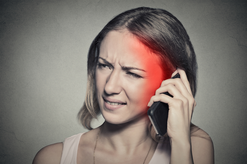 girl on the phone with headache. Upset unhappy female talking on phone isolated grey wall background. Negative human emotion face expression feeling life reaction. Cellular mobile radiation concept